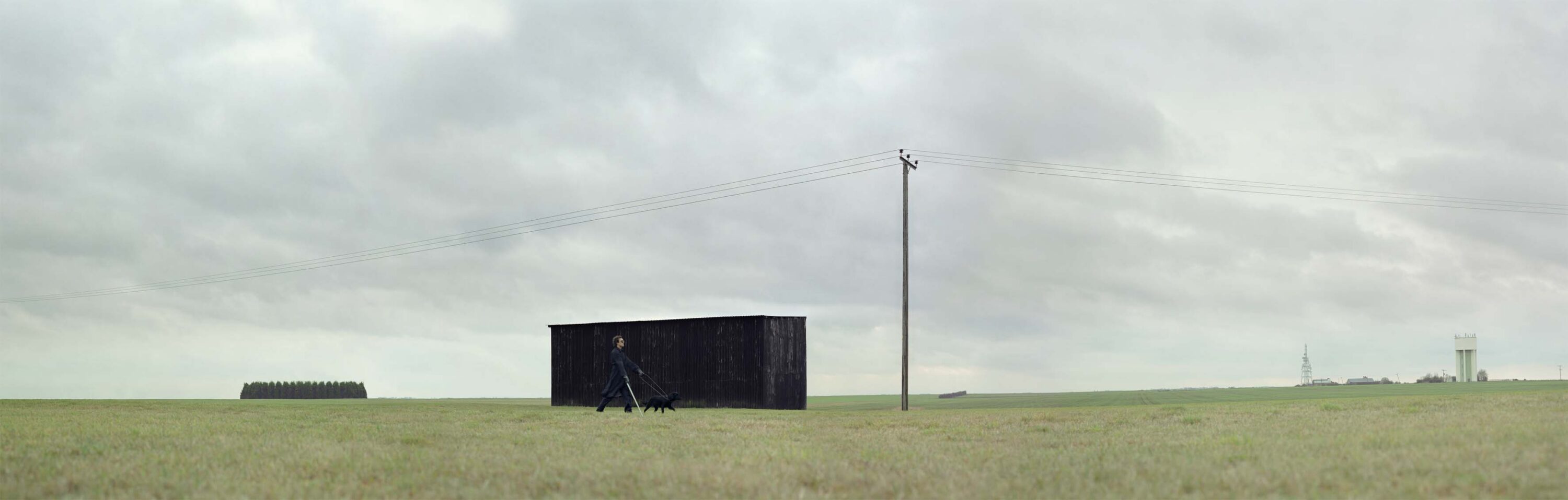 Black dog leads black coat past black shed